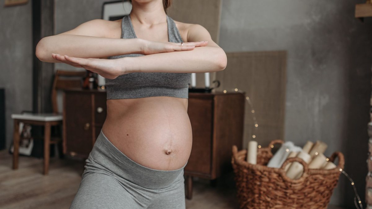 Fit pregnant woman doing yoga indoors, focusing on health and flexibility.